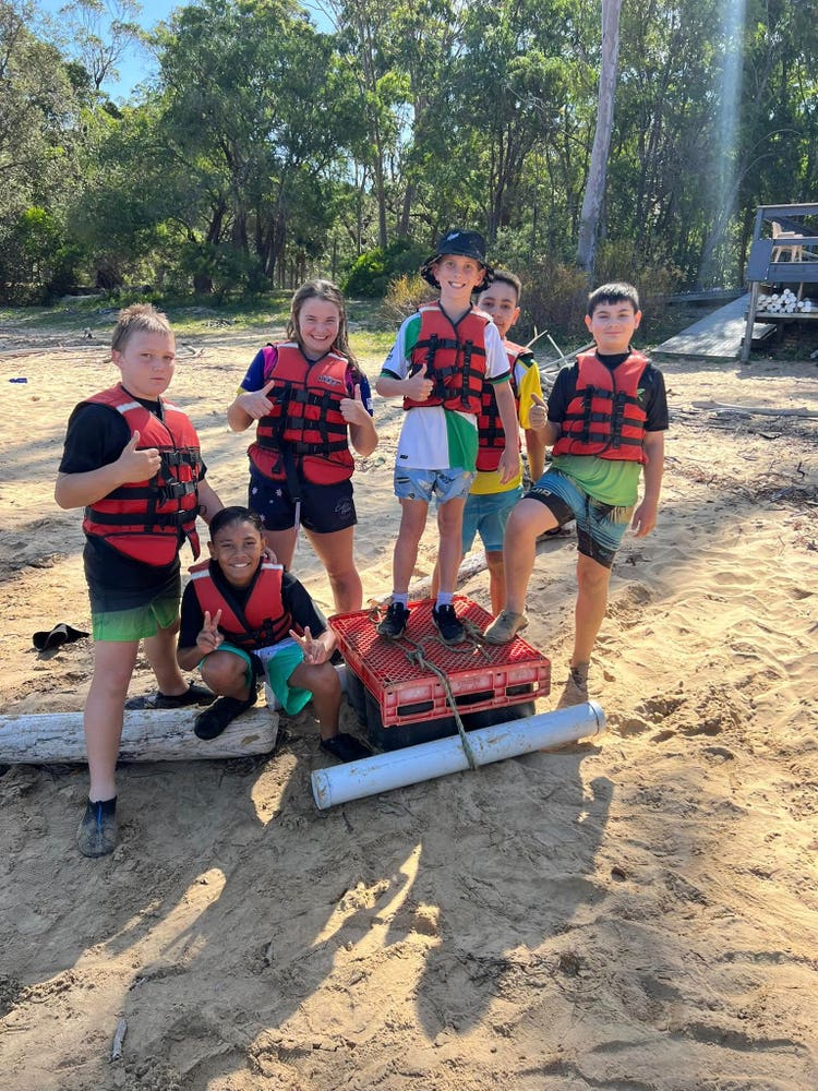 6 students raft building on the sand, at camp