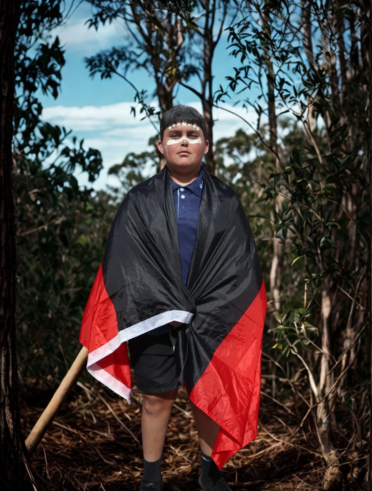 boy drapped in Aboriginal Flag with ochre face paint