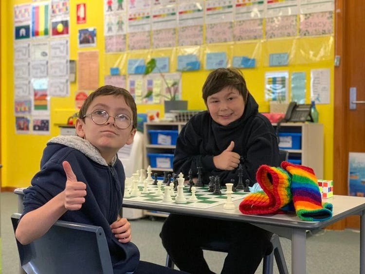 2 boys with thumbs up playing chess